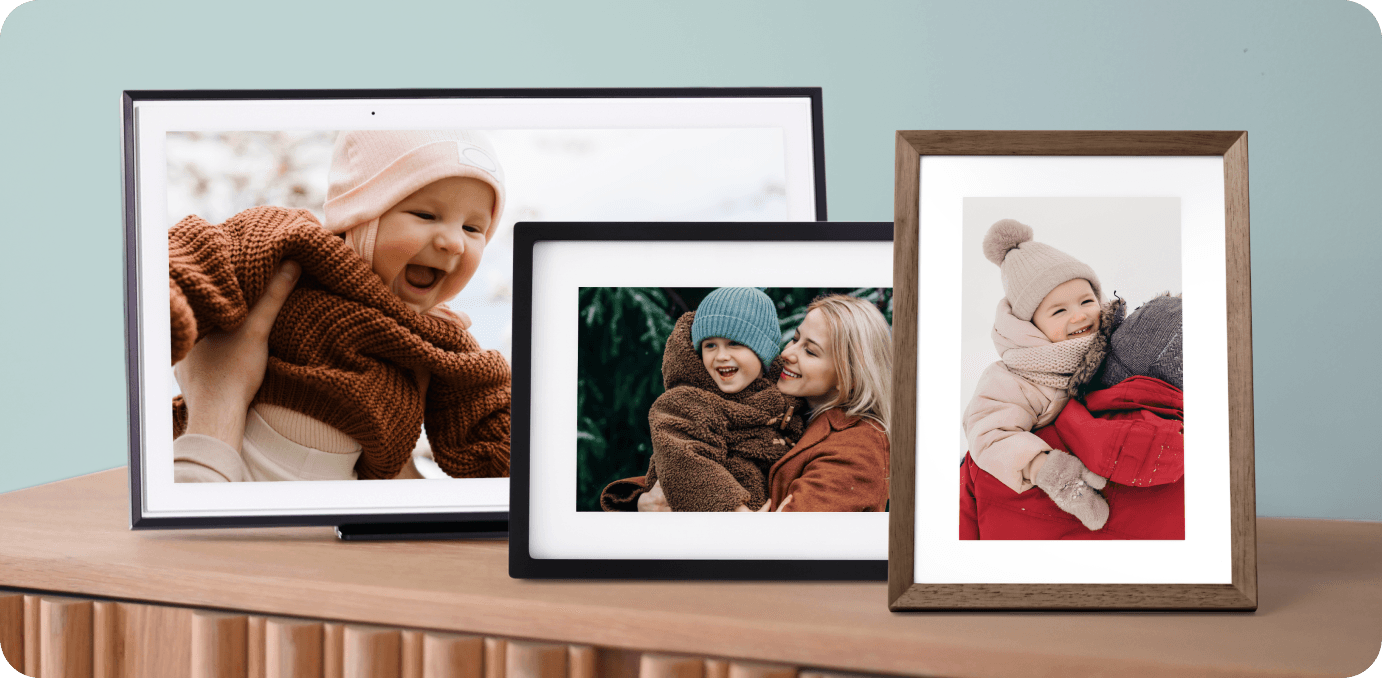 Three frames of different sizes and colors on a desk each with a different family photo including a smiling baby